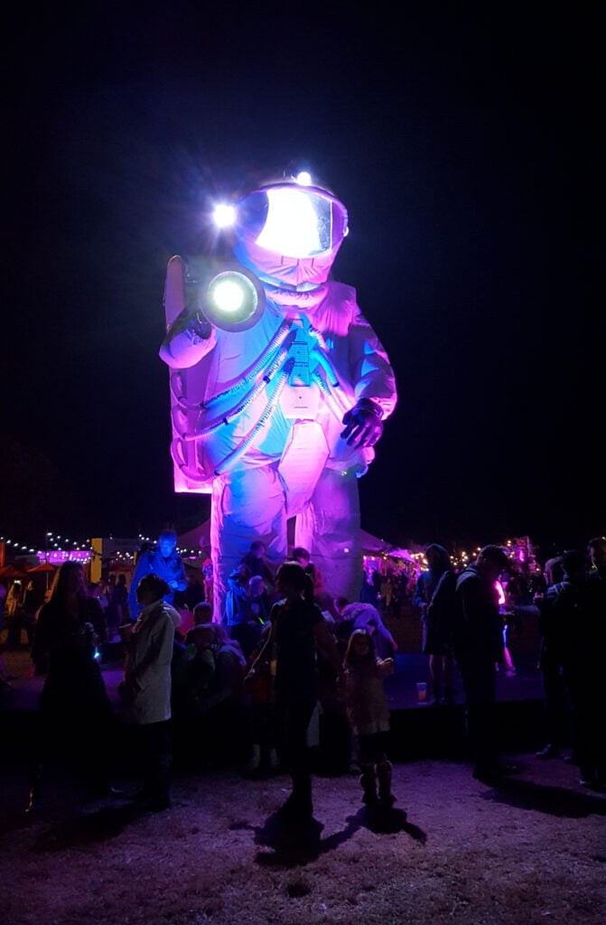 A giant astronaut, glowing purple and blue, towers above the crowd after dark
