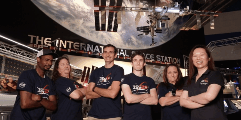 Team ISS posing in NASA t shirts in front of the ISS mimic