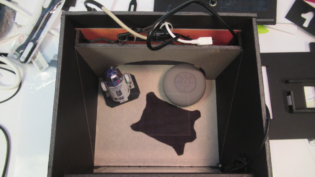 A piece of clear acrylic is placed at a 45 degree angle to the top of the box so that it can reflect the video onto the speaker/table