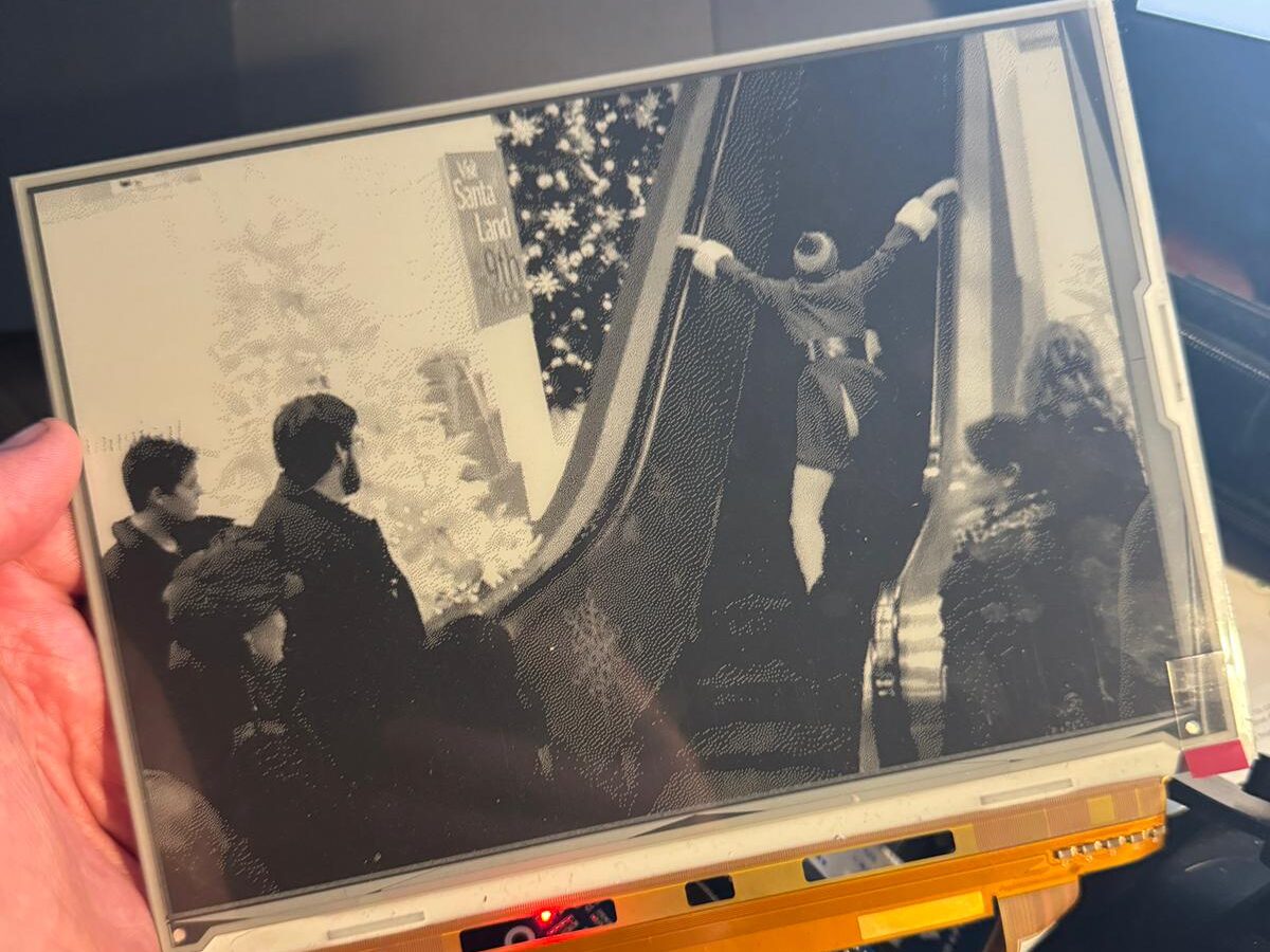 Buddy the Elf stretching into a split on a moving escalator in black and white on an e paper display