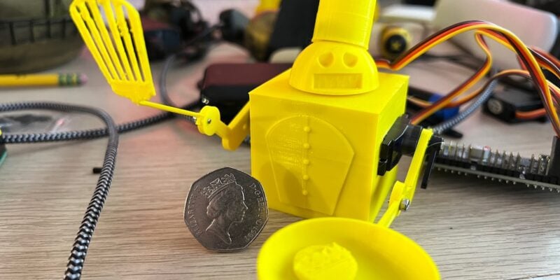 bright yellow 3d printed boxy bodied chef holding a spatula and a frying pan. looks a bit angry