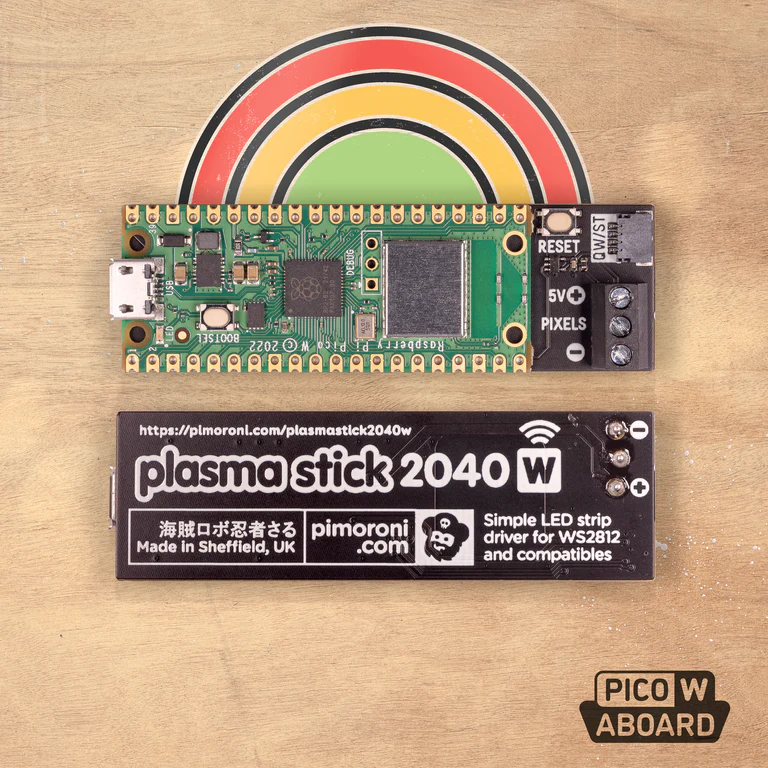 a raspberry pi pico w laying flat on a brown wooden table with a rainbow sticker on top of it. under the pico is a black plasma stick 2040 w featuring the pimoroni logo