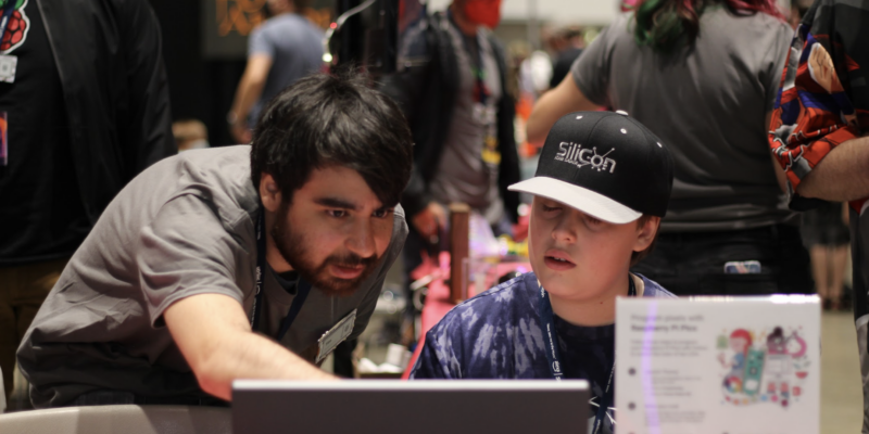 tim is bent over a computer work station showing a child in a baseball hat how to code lEDs