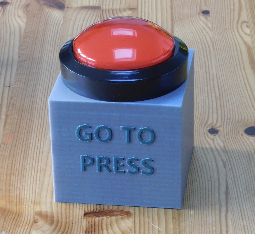  a large red button.
Setting: The button is mounted on a grey box with visible wires, suggesting it’s part of an electrical system.
Text: “GO TO PRESS” is indicated on the box, which may imply the button initiates a process or action.
The background is plain, featuring what seems to be a white wall and a section of a table or counter. The image captures a moment of interaction with a device that likely serves a specific function, possibly in an industrial or mechanical context.